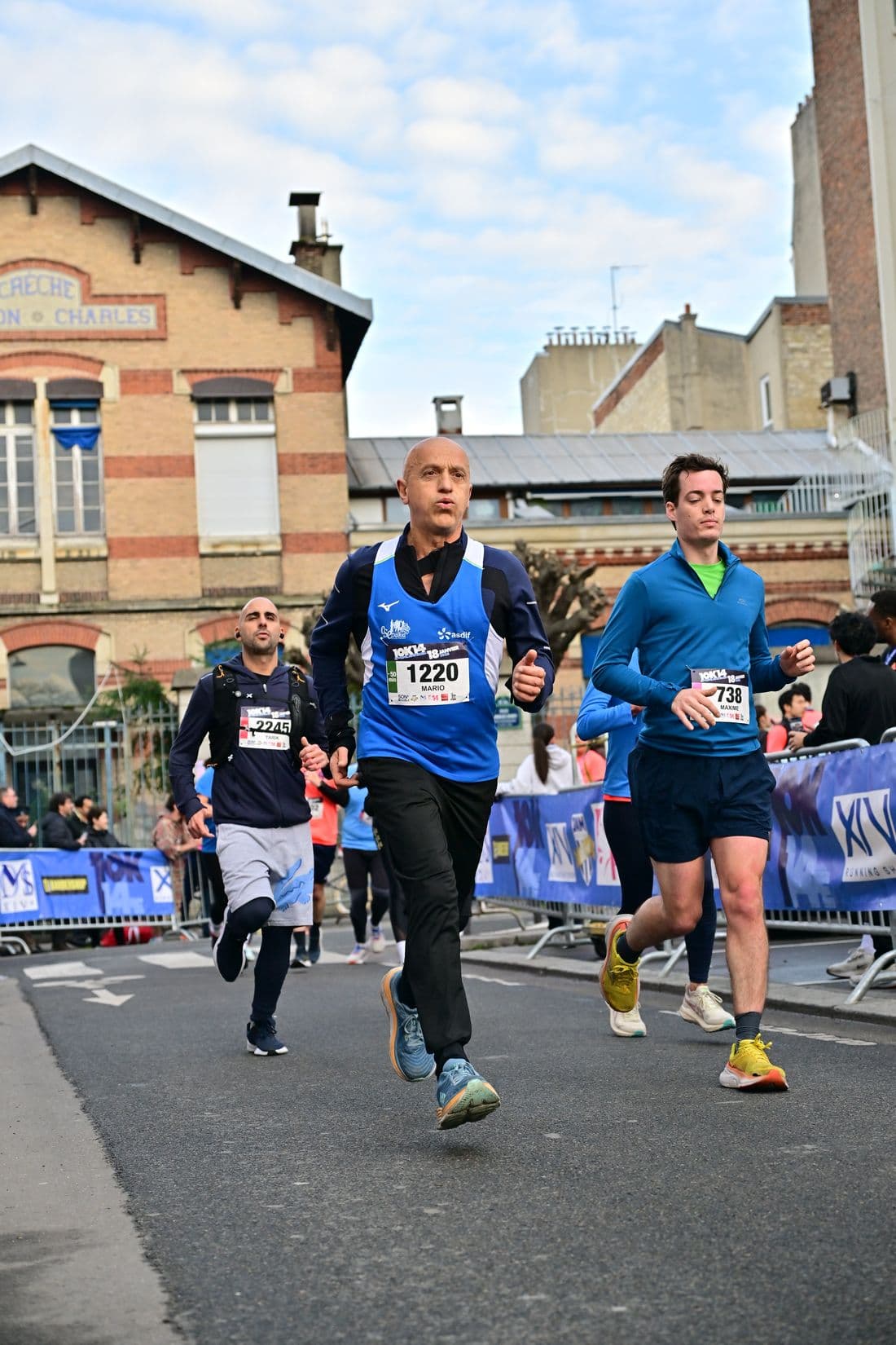 Course sur route en ville, trois dossards lus sur une seule photo dont un coureur en arrière-plan
